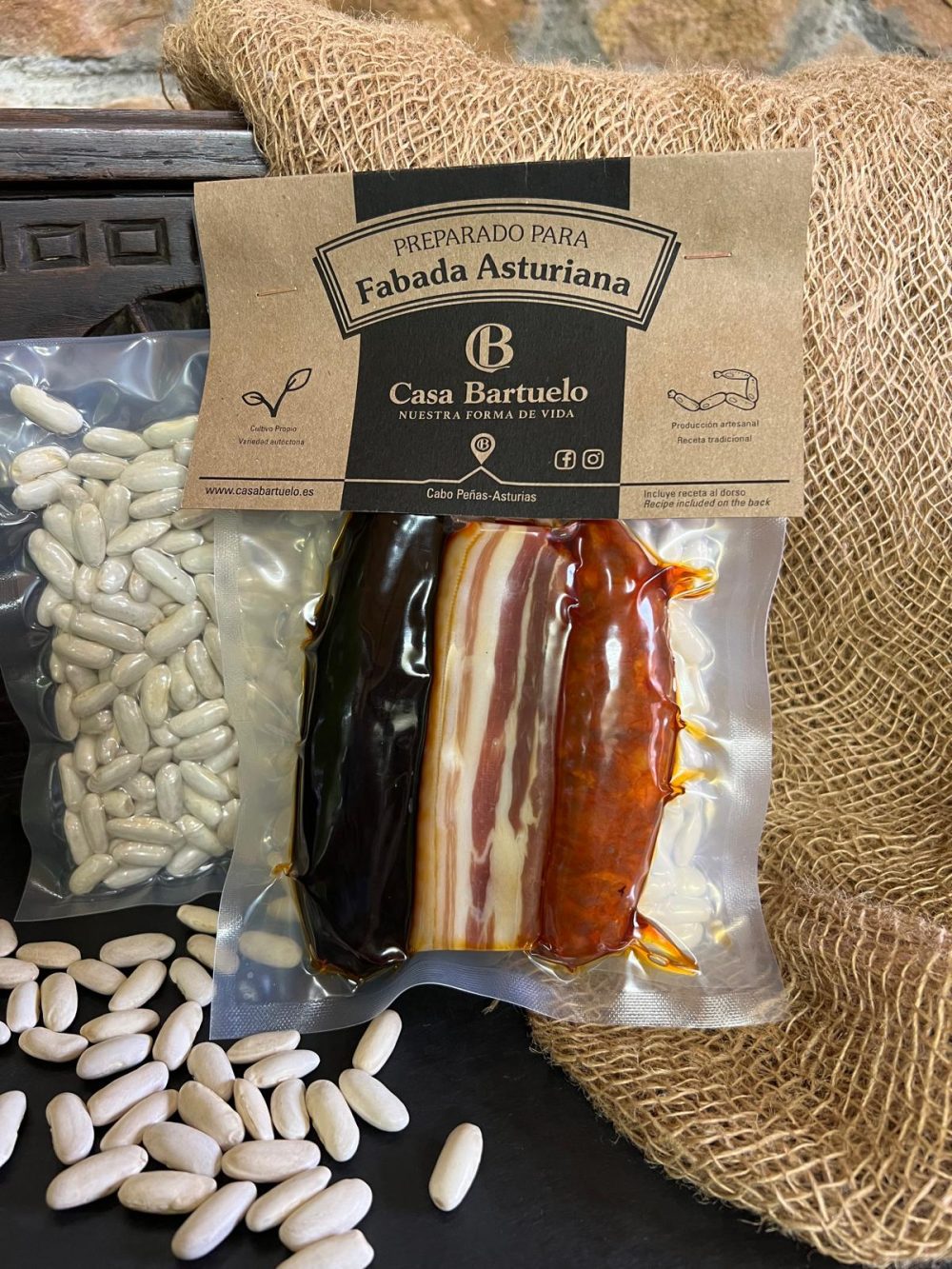 En la foto se muestran dos bolsas que forman el producto de venta: el preparado de fabada. A la izquierda está la bolsa con la faba, y a la derecha está el compango.